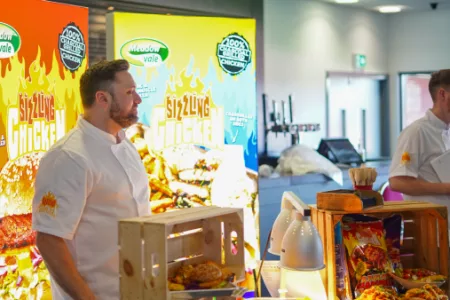 Two men stand in front of a large food display, showcasing a variety of dishes and culinary delights.